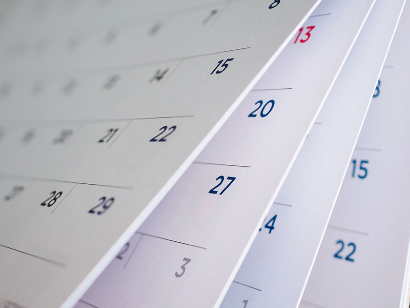 Close-up of calendar pages flipping, showing dates in bold blue and red text, symbolizing scheduling, planning, or upcoming events.